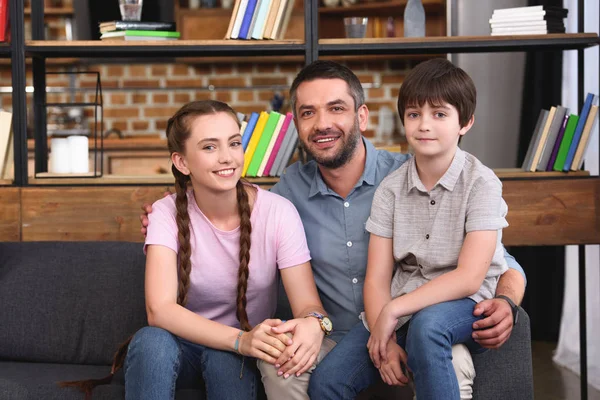 Selective focus of happy father embracing teenage daughter and little son on sofa at home — Stock Photo