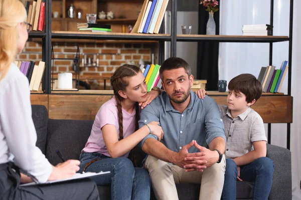 Children cheering up father while he talking to female counselor on therapy session — Stock Photo