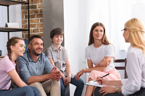 Happy family sitting on therapy session by female counselor writing in clipboard in office — Stock Photo