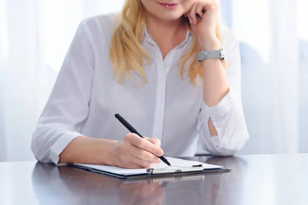 Обрезанное изображение женщины-консультанта, пишущей в буфер обмена за столом в офисе — стоковое фото