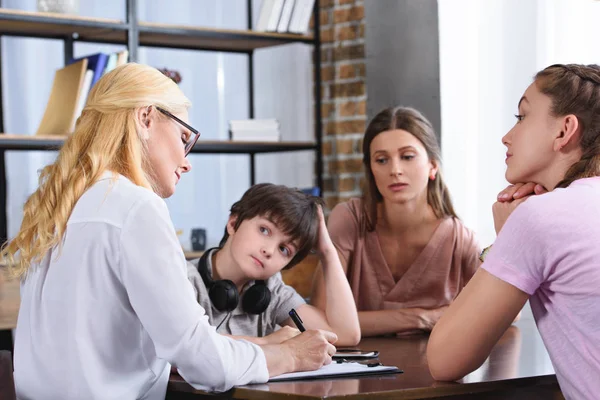 Consejera femenina escribiendo en portapapeles sobre la sesión de terapia con la familia en la oficina - foto de stock