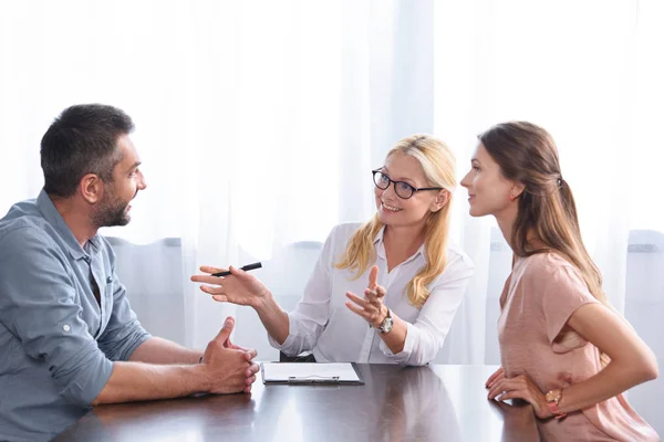 Lächelnde Beraterin gestikuliert mit den Händen und spricht mit Paar bei Therapiesitzung im Büro — Stockfoto