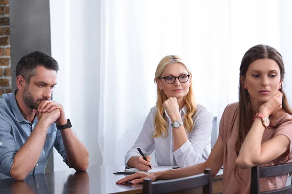 Woman turned away and her frustrated husband sitting at table on therapy session by female counselor in office — Stock Photo