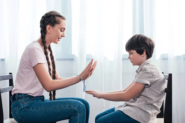 Seitenansicht von Bruder und Schwester beim Spielen, während sie zu Hause auf Stühlen sitzen — Stockfoto