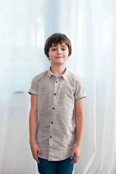 Little smiling boy looking at camera in front of curtains at home — Stock Photo