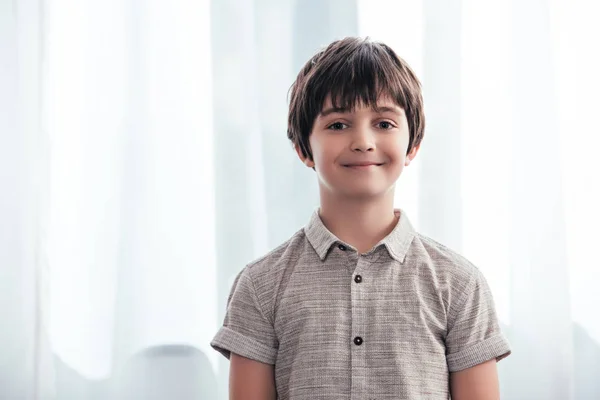 Porträt eines lächelnden kleinen Jungen, der zu Hause vor Vorhängen in die Kamera blickt — Stockfoto