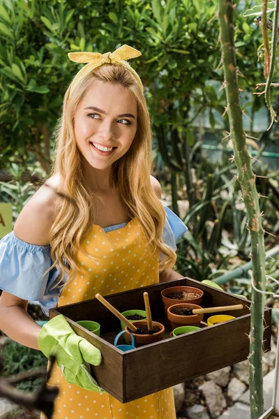 Красивая улыбающаяся женщина держит коробку с цветочными горшками и смотрит в оранжерею — стоковое фото