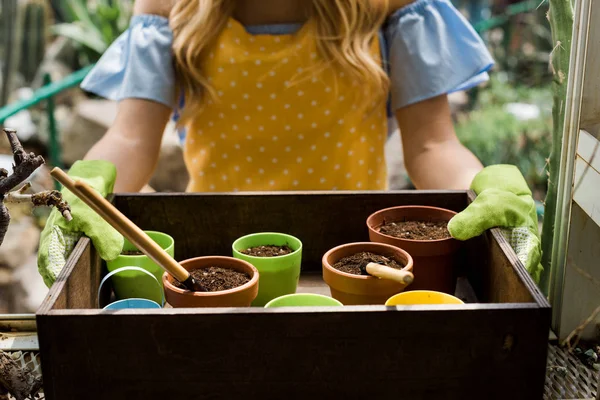 Plan recadré de jeune femme dans des gants en caoutchouc tenant boîte avec des pots, de la terre et des outils de jardinage — Photo de stock