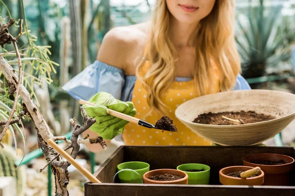 Обрізаний знімок молодої жінки, що працює з грунтом і квітковими горщиками в теплиці — стокове фото