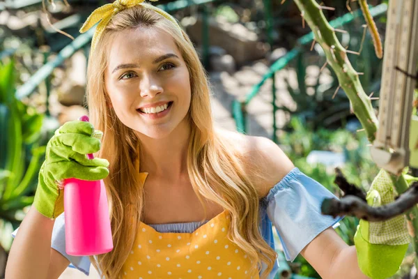 Schöne lächelnde junge Frau hält Sprayer im Gewächshaus — Stockfoto