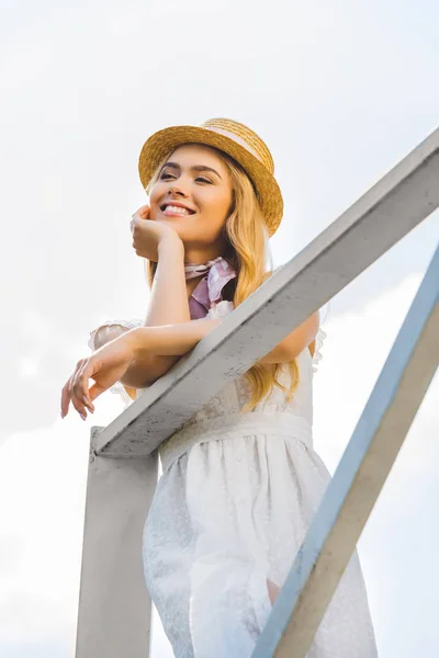 Vue à angle bas de fille blonde heureuse penchée sur une rampe en bois et regardant loin — Photo de stock