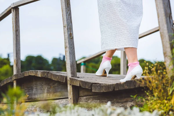 Обрезанный снимок женщины в белом платье идущей по деревянному пешеходному мосту — стоковое фото
