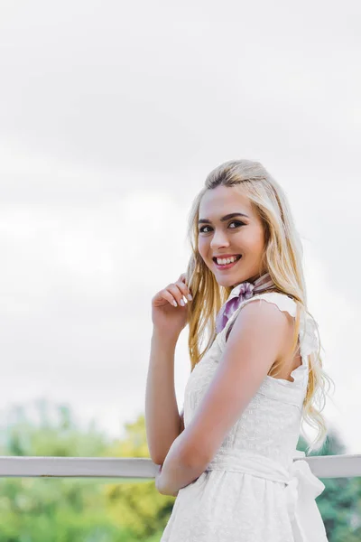 Hermosa joven rubia en vestido blanco sonriendo a la cámara - foto de stock