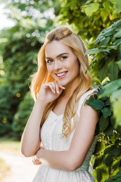 Beautiful young blonde woman in white dress smiling at camera — Stock Photo