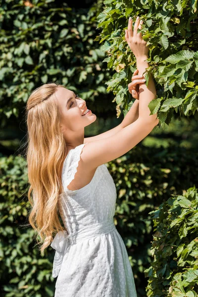 Side view of beautiful happy girl touching green leaves — Stock Photo