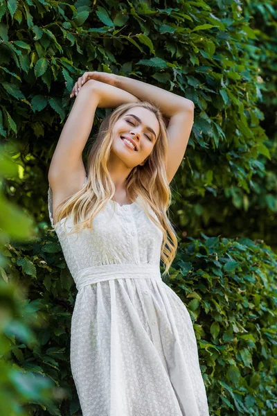 Belle fille blonde heureuse posant avec les yeux fermés près des feuilles vertes — Photo de stock