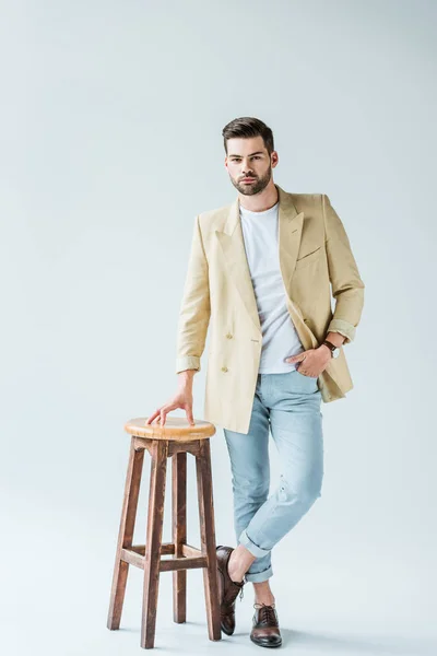 Homem confiante na moda apoiando-se nas fezes no fundo branco — Fotografia de Stock