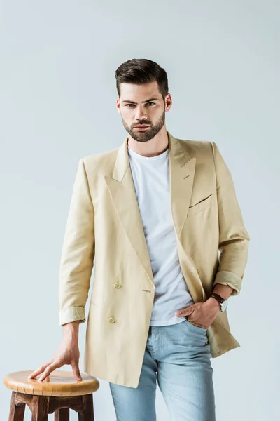 Uomo alla moda fiducioso in piedi da sgabello isolato su sfondo bianco — Foto stock