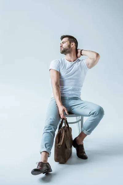 Красивый бородатый мужчина сидит на стуле и держит портфель на белом фоне — стоковое фото