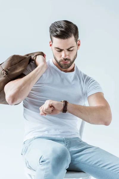 Hombre barbudo guapo sosteniendo maletín y revisando su reloj aislado sobre fondo blanco - foto de stock