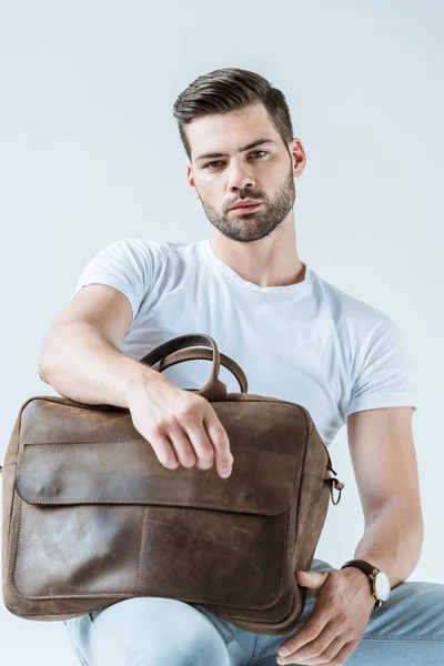 Стильний молодий чоловік сидить і тримає портфель ізольовано на білому тлі — стокове фото
