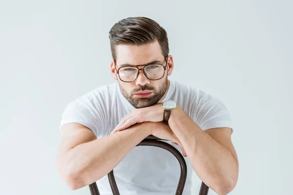 Elegante giovane uomo in occhiali seduto sulla sedia isolato su sfondo bianco — Foto stock