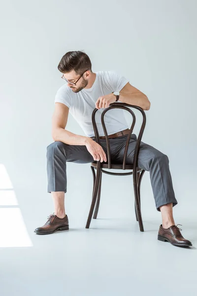 Modisch selbstbewusster Mann mit Brille sitzt auf Stuhl auf weißem Hintergrund — Stockfoto