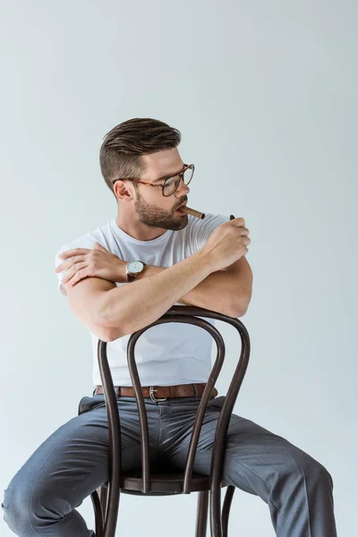 Hombre barbudo guapo encendiendo su cigarro mientras está sentado en la silla aislado sobre fondo blanco - foto de stock