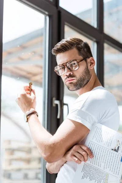 Stylish young man holding cigar and standing by window — Stock Photo