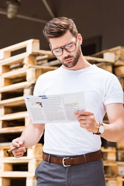 Hombre de negocios barbudo guapo sosteniendo cigarro y leyendo informe por paletas de madera - foto de stock