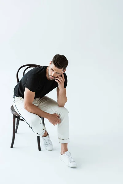 Jovem elegante sentado na cadeira no fundo branco — Fotografia de Stock