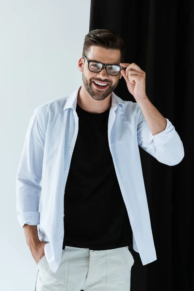 Elegante jovem sorrindo e vestindo óculos de pé por cortina preta — Fotografia de Stock