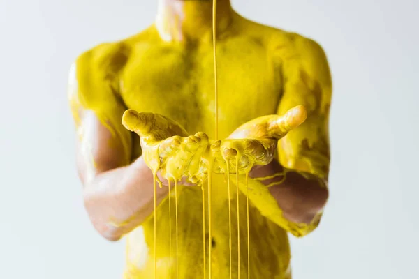 Vue recadrée de la peinture jaune coulant sur les mains masculines isolées sur fond blanc — Photo de stock