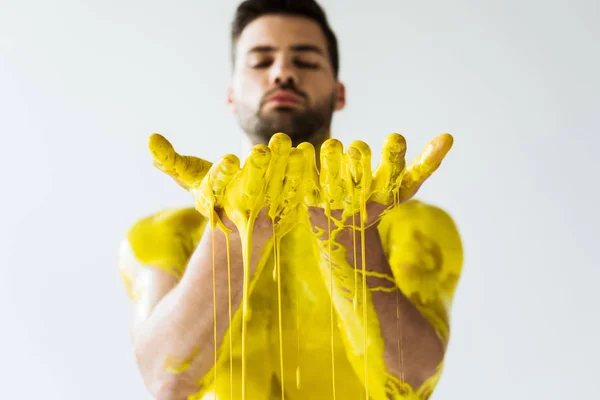 Foco seletivo de mãos masculinas com tinta amarela fluente isolada no fundo branco — Fotografia de Stock