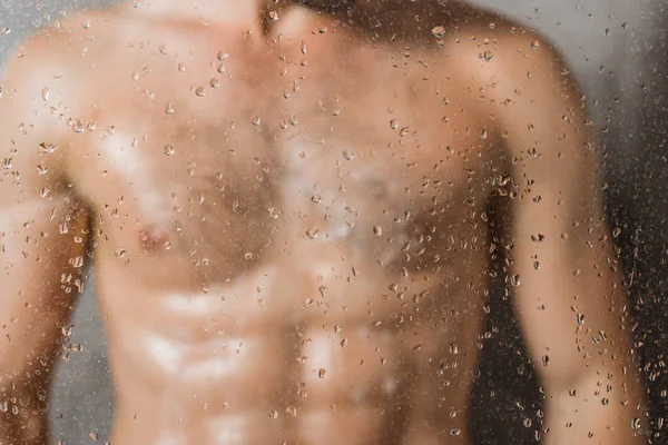 Borrosa a través de la vista de cristal del hombre tomando la ducha - foto de stock