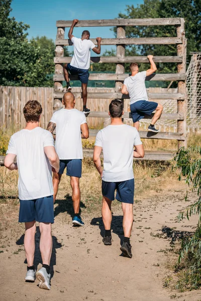 Vue de dos des soldats multiculturels pratiquant la course d'obstacles sur le champ de tir le jour d'été — Photo de stock