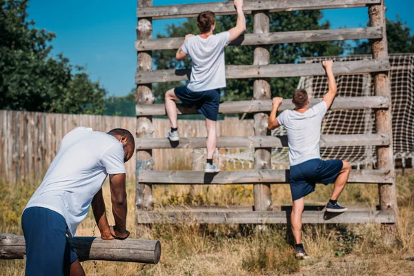 Vista posteriore dei soldati multiculturali che praticano corsa ad ostacoli a portata di mano nella giornata estiva — Foto stock