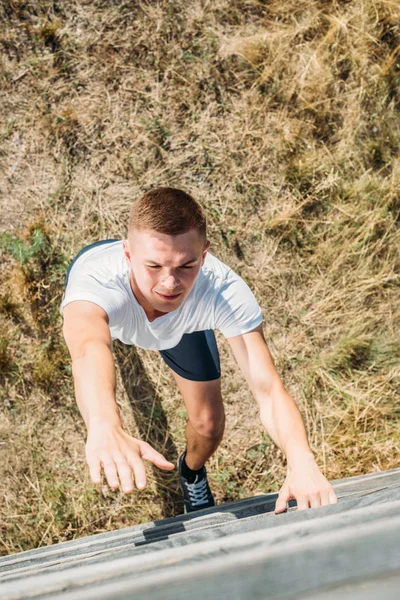 Visão aérea do jovem soldado escalando barreira de madeira durante o percurso do obstáculo no alcance — Fotografia de Stock