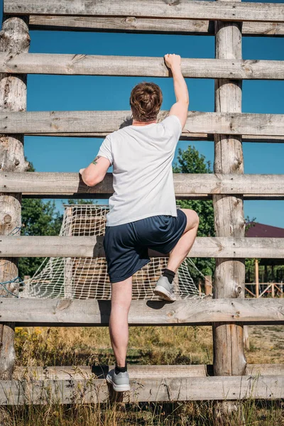 Vista trasera del soldado escalando la barrera de madera durante la carrera de obstáculos en rango - foto de stock