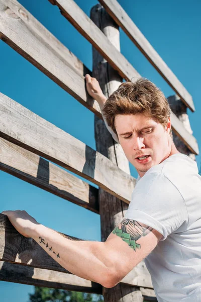 Side view of young soldier climbing wooden barrier during obstacle run on range — Stock Photo