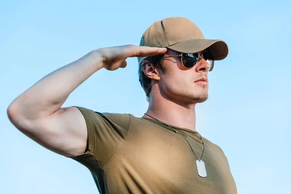 Vista lateral do jovem soldado em boné e óculos de sol contra o céu azul — Fotografia de Stock