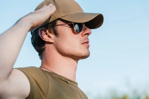 Вид сбоку молодого солдата в кепке и солнцезащитных очках на фоне голубого неба — стоковое фото