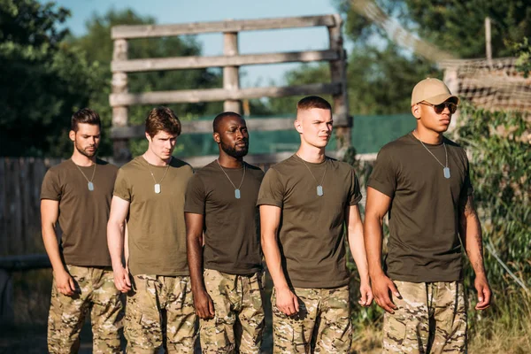 Multiethnic group of young soldiers in military uniform with tag dogs standing on range — Stock Photo