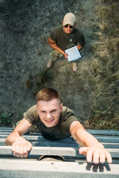 Vue aérienne d'un instructeur tactique afro-américain avec bloc-notes examinant un jeune soldat pendant une course à obstacles — Photo de stock