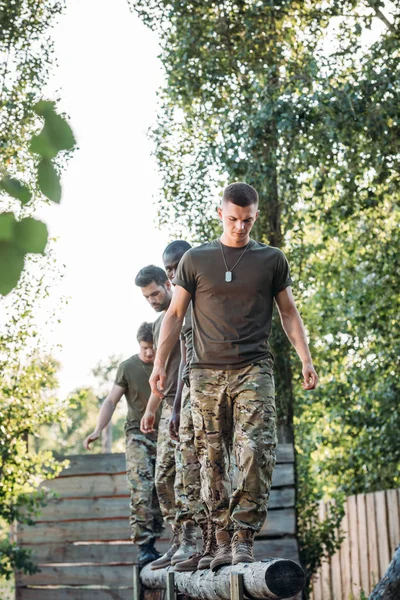 Foco seletivo de soldados multiétnicos em uniforme militar praticando em obstáculo executado em alcance — Fotografia de Stock