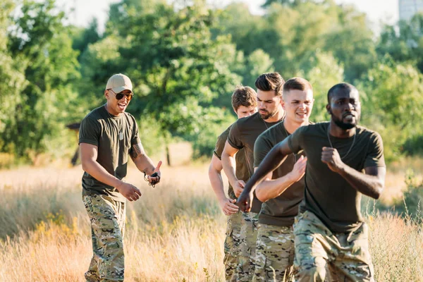Instructeur tactique afro-américain avec chronomètre examinant les soldats multiraciaux pendant la course d'obstacles à portée — Photo de stock