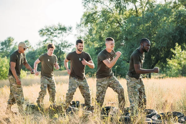 Side view of interracial soldiers practicing with tires on ground on range — Stock Photo