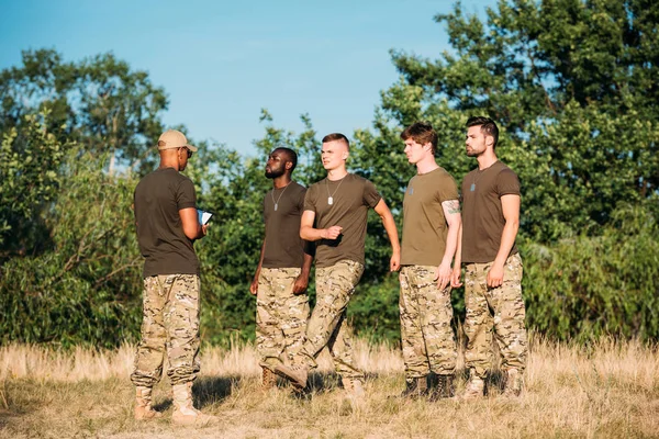 Instructeur tactique afro-américain avec bloc-notes et jeunes soldats multiethniques à portée — Photo de stock