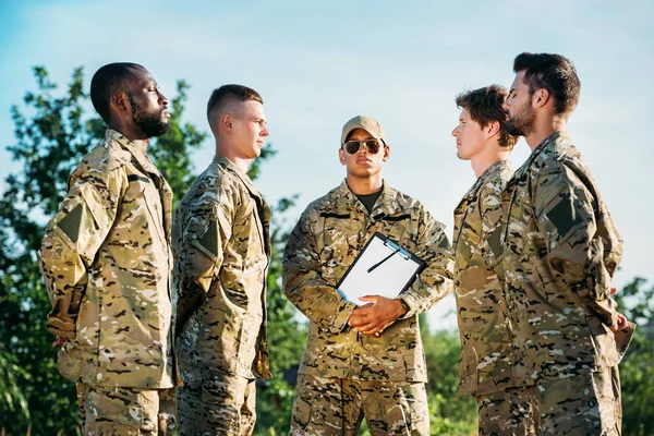 African american tactical instructor with notepad and young interracial soldiers in military uniform on range — Stock Photo