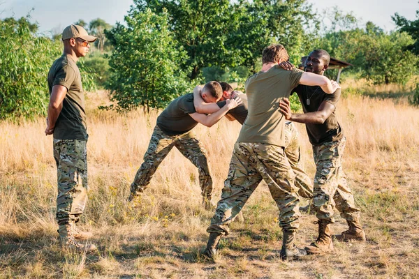 Multiracial soldiers in military uniform practicing hand to hand fighting on range — Stock Photo